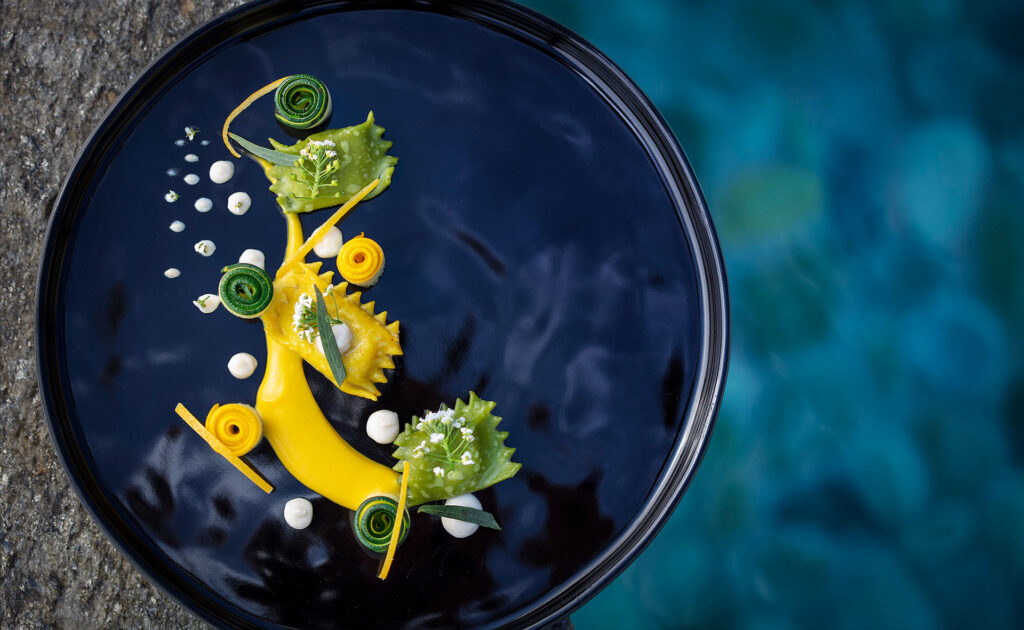 A tasting course at Sierra Mar, herb-flecked green parcels and coiled ribbons of squash set along a swipe of golden puree on a black lacquered plate.